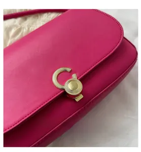 Close-up of a rose red leather shoulder bag featuring a golden textured rotary lock