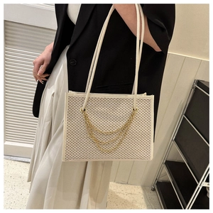 Detail of cream woven straw tote featuring triple layered gold metal chains and textured finish