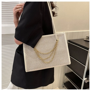 Detail of cream woven tote bag with triple gold chain accents and textured pattern