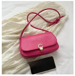 Detail of fuchsia underarm bag with metal buckle and knot strap next to a mobile phone