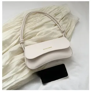 Détail du sac sous le bras en similicuir crème avec logo doré et fine bandoulière
