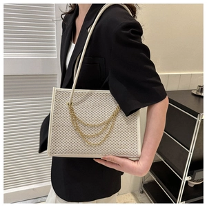 Close-up of woven straw bag detail featuring triple gold chain decor and white leather trim