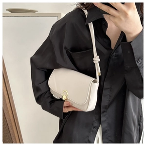 Detail of a creamy white underarm bag featuring a golden circular twist lock and knot strap