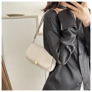 Detailed shot of cream underarm bag featuring a gold ring clasp on black silk shirt