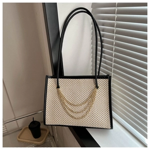 Detailed close-up of large straw tote bag with black leather handles and gold chain details