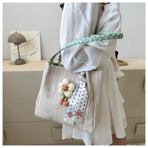 Détail d'un sac cabas en paille beige avec anses tressées vertes et pendentif floral