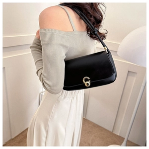 Detail of minimalist black leather underarm bag with gold ring clasp and knotted strap