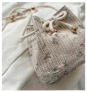 Detail of beige woven bucket bag featuring floral embroidery and white drawstring closure