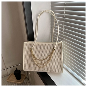 Close-up of cream woven tote with triple gold chain details in soft window light