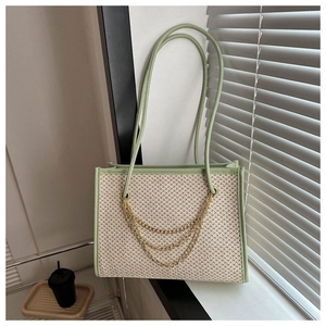Detail of woven straw tote bag featuring green leather trim and decorative gold chains