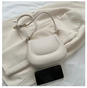 Detail of cream saddle bag with textured leather, gold hardware on blazer background
