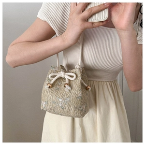 Close-up of woven straw bucket bag with blue floral embroidery and drawstring detail