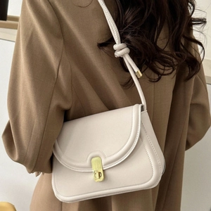 Minimalist beige saddle bag with gold metal clasp and knot strap on a shoulder