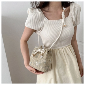 Detailed close-up of woven bucket bag with floral embroidery and white drawstring closure