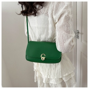 Macro shot of green leather shoulder bag featuring a gold C-shaped metal buckle on the flap