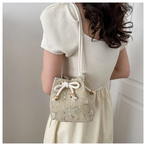 Detail of woven bucket bag featuring floral embroidery and cotton drawstring closure