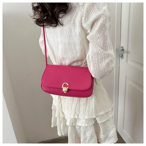 Detail of fuchsia leather crossbody bag with golden C-lock worn over white lace dress