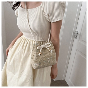 Detail of floral embroidery on beige woven bucket bag with cotton drawstring and metal buckle