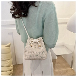 Close-up of woven bucket bag featuring floral embroidery and white bow drawstring detail