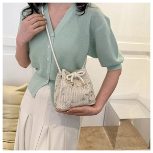Close-up of woven bucket bag featuring green floral embroidery and drawstring closure