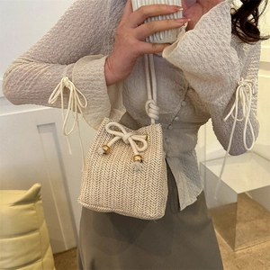 Minimalist hand-woven straw bucket bag in cream white with stylish gold metal accents