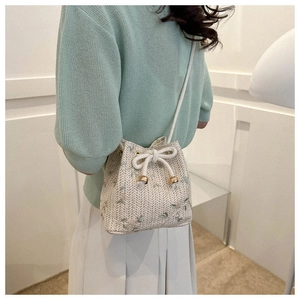 Detail of cream woven bucket bag with green floral embroidery and gold bead drawstrings