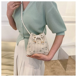 Detail of woven straw bucket bag with floral embroidery and white drawstring strap