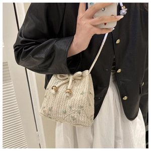 Detail of woven bucket bag with green leaf embroidery and white drawstring closure