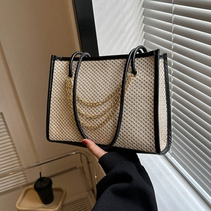 Large straw tote bag with black leather trim and gold chain detail for summer