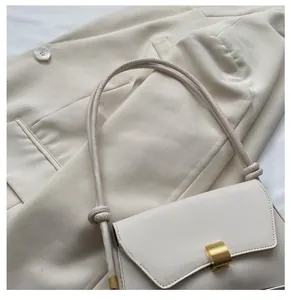 Detail of cream flap handbag with matte gold lock and knotted strap on blazer