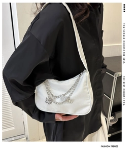Detailed view of white half-moon shoulder bag with silver chains and butterfly charm