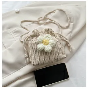 Detail view of mini woven straw bucket bag with white crochet flower and drawstring close