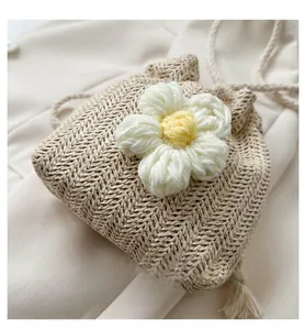 Detail of beige woven drawstring bucket bag with a white knit flower and twisted shoulder strap