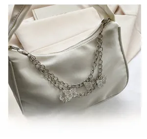 Close-up of double metal chains with hollow butterfly charms on a cream shoulder bag