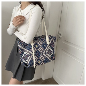 Ethnic style woven canvas tote bag shown worn on shoulder with leather handles
