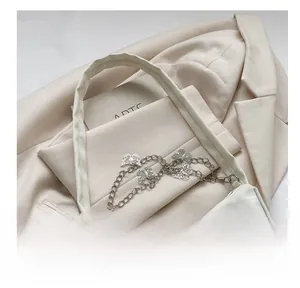 Detail of minimalist cream shoulder bag with decorative silver butterfly metal chain