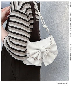 Close-up of white bow shoulder bag featuring pearl chain and clover metal accents