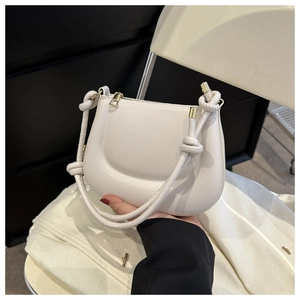 Close-up of cream saddle bag featuring a knotted handle and golden zipper detail