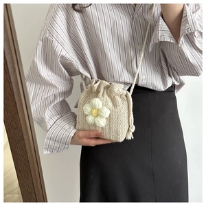 Close-up of mini straw bucket bag with white knit daisy flower and woven shoulder strap
