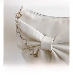 Close-up of white fashion handbag featuring a large bow and pearl flower metal chain