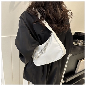 Close-up of white half-moon bag featuring silver chains and delicate metal butterfly charms