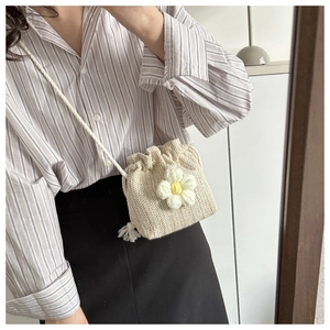 Detail of hand-woven off-white bucket bag with 3D floral accent and rope strap