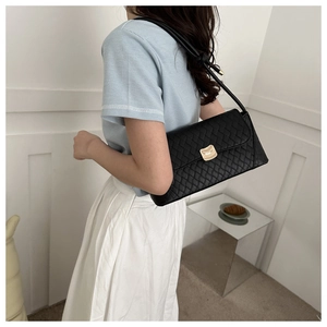 Close-up of a stylish black quilted leather baguette bag with a golden metal lock