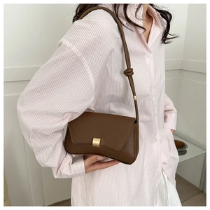 Detail of retro brown leather baguette bag featuring a matte gold square lock and knot strap