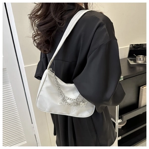 Close-up of white satin baguette bag with silver butterfly chain charms on shoulder