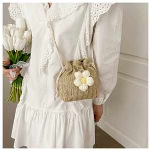 Detail view of woven straw bucket bag with white crochet flower and drawstring closure