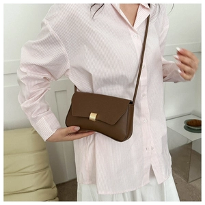 Detail of dark brown leather baguette bag with gold buckle and slim leather strap