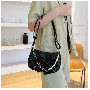Detail of black bow shoulder bag with pearl accents and floral chain on a model