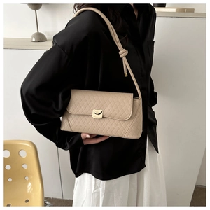 Macro detail of beige quilted baguette bag featuring a gold buckle and knotted shoulder strap