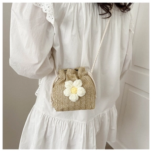 Detail of hand-woven straw bucket bag with knit flower accent and drawstring strap